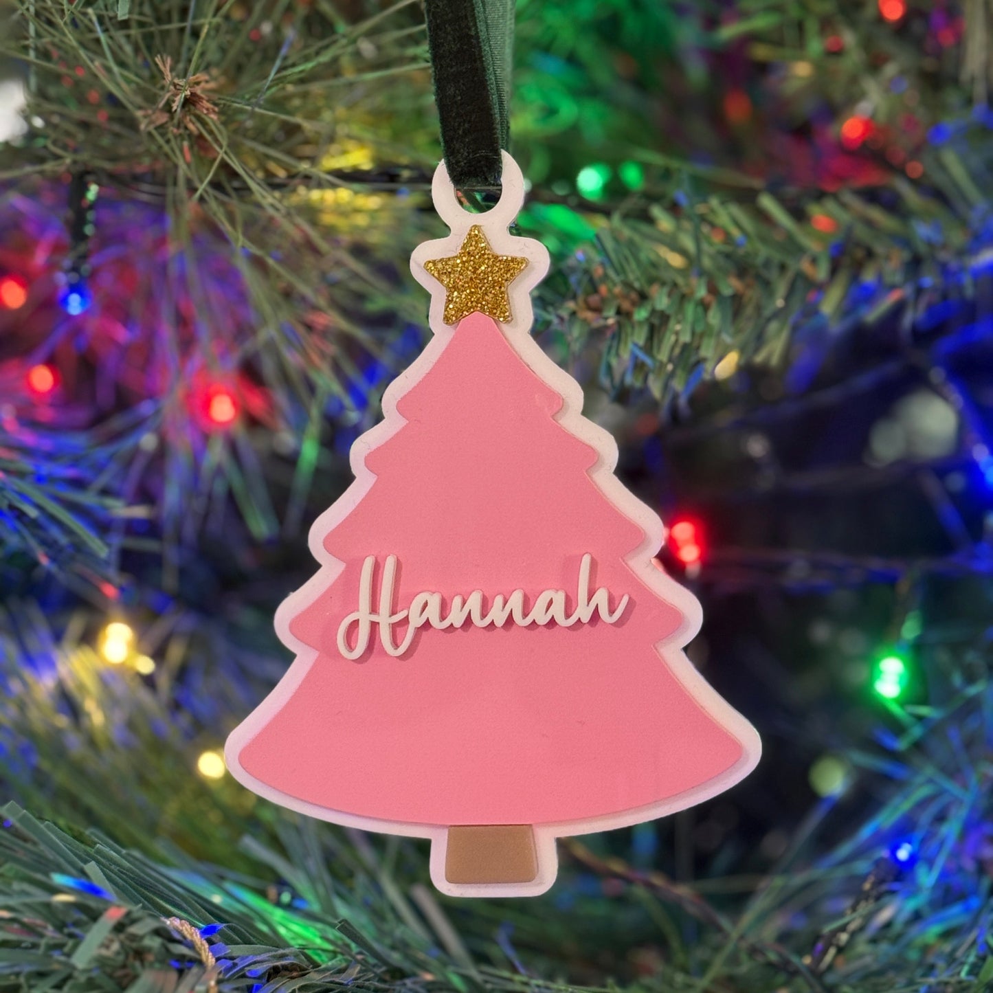 Pink Christmas tree-shaped ornament with 'Hannah' on a decorated tree