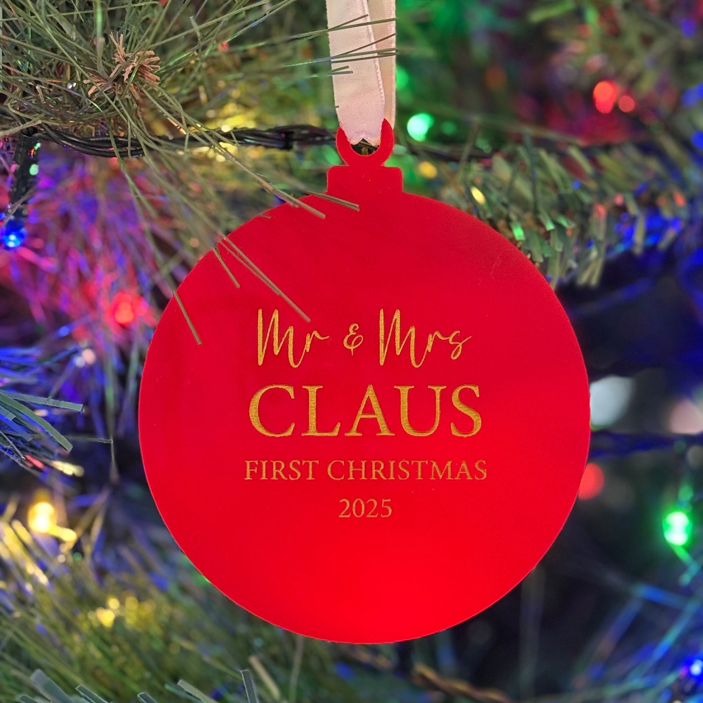 Red ornament with 'Mr & Mrs Claus First Christmas 2025' text on a Christmas tree.